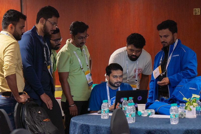 A group huddled around a laptop, working through a problem together